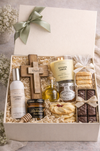Gift box with various items including a candle, cross, and cookies on a neutral background