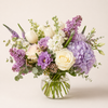 Bouquet of purple and white flowers in a clear vase on a light background