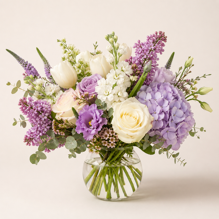 Bouquet of purple and white flowers in a clear vase on a light background