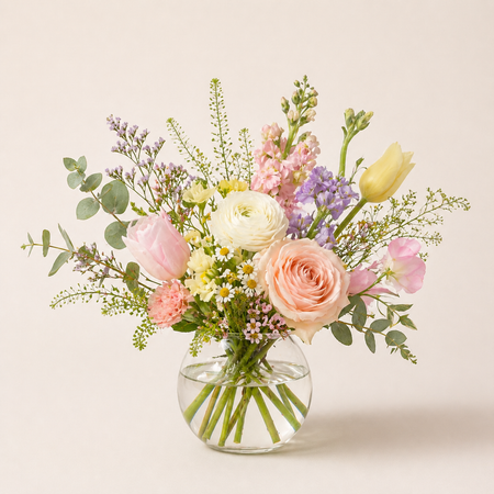 Bouquet of pastel flowers in a clear vase on a light background