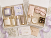 Gifting set with skincare products, a candle, and a sleep mask on a marble surface.