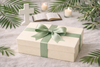 Gift box with a green ribbon on a table with candles and a cross
