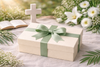 Gift box with a green ribbon on a table with flowers and a cross in the background