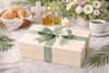 Gift box with a green ribbon on a table with a cup of tea, bread, and flowers.