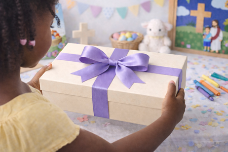Child holding a gift box with a purple ribbon in a classroom setting