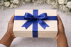 Gift box with a blue ribbon held by hands against a blurred floral background