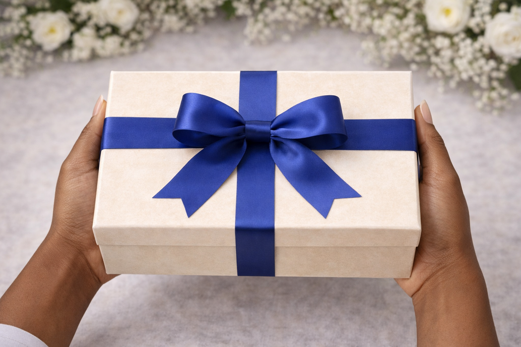 Gift box with a blue ribbon held by hands against a blurred floral background