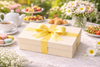 Gift box with a yellow ribbon on a table with tea and pastries