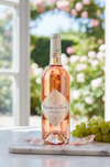 Bottle of Château de Fleurs Rosé Provençal wine on a table with grapes and flowers in the background.